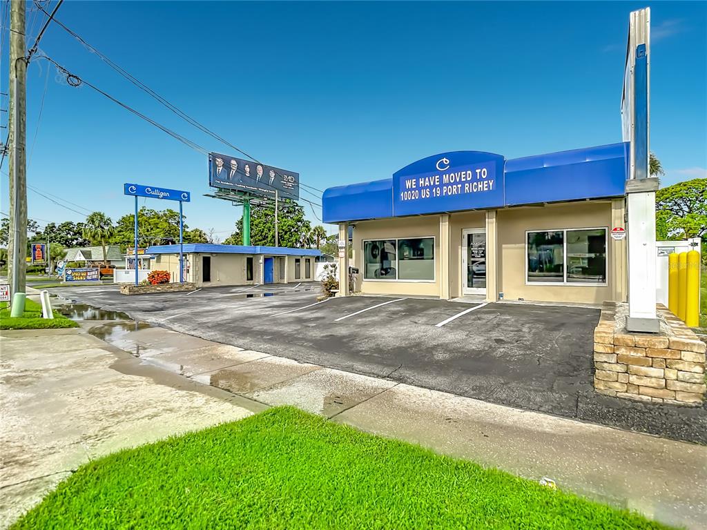 A commercial building with a blue awning and a paved parking lot under a clear sky — 7429 US HIGHWAY 19, NEW PORT RICHEY, FL