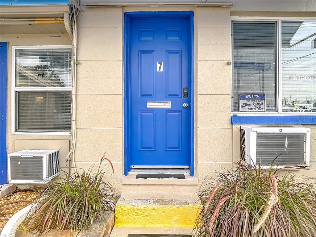 A bright blue front door with the number seven sits between two windows and air conditioners — 7429 US HIGHWAY 19, NEW PORT RICHEY, FL