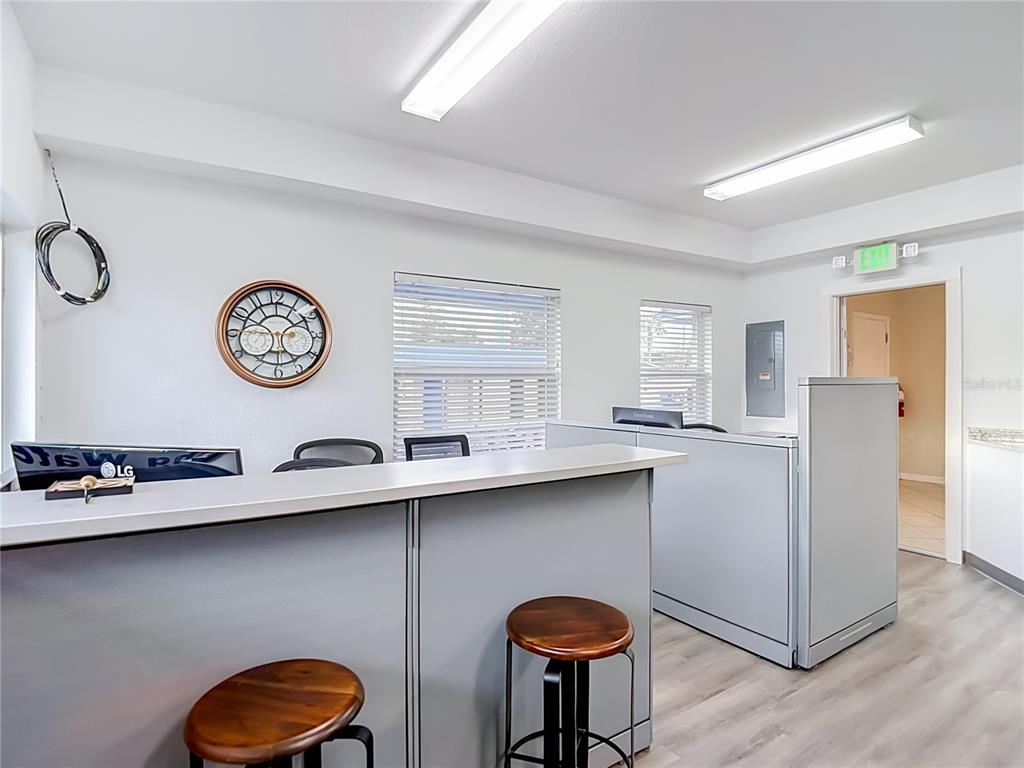 An office reception area features a grey counter, two wooden stools, and a wall clock — 7429 US HIGHWAY 19, NEW PORT RICHEY, FL