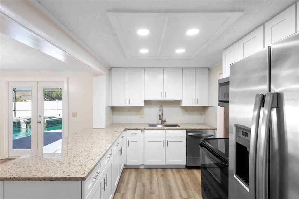 A kitchen features white cabinets, granite countertops, stainless steel appliances, and a view of a pool — 3307 CALDWELL STREET, DELTONA, FL