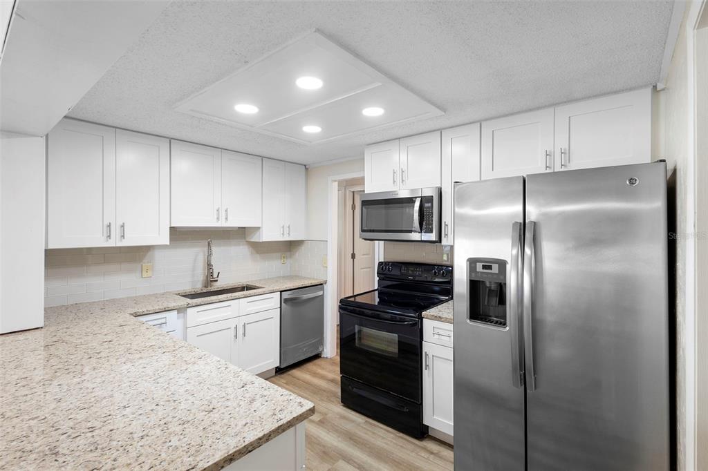A kitchen features white cabinets, granite countertops, stainless steel appliances, and a black range — 3307 CALDWELL STREET, DELTONA, FL