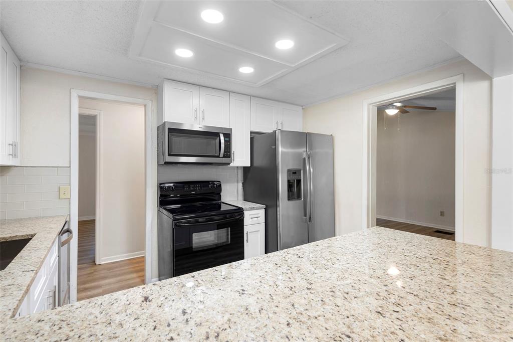 A kitchen features white cabinets, stainless steel appliances, and a granite-topped island — 3307 CALDWELL STREET, DELTONA, FL