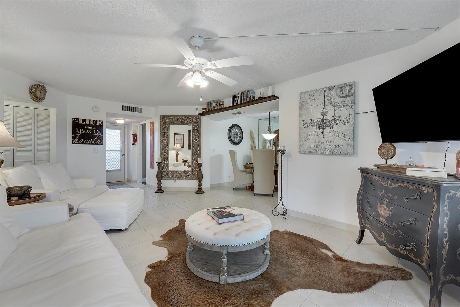A living room features white sofas, a tufted ottoman, a cowhide rug, and a television — 3755 Via # 405, Lake Worth FL 33467, LAKE WORTH, FL