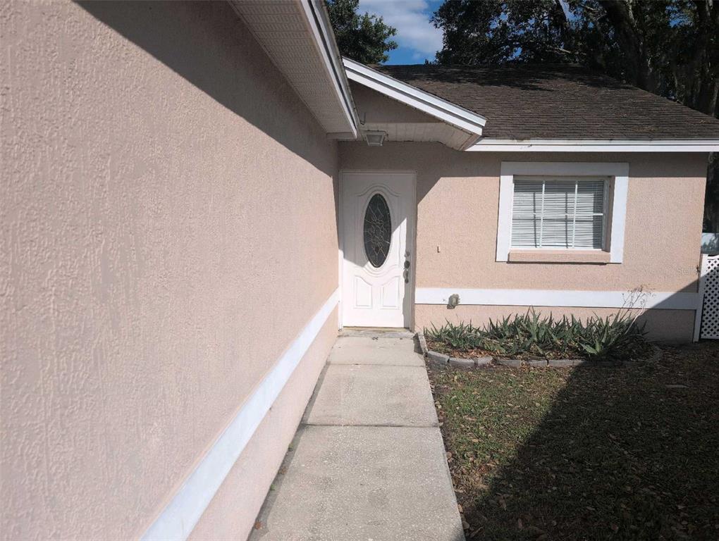 A concrete walkway leads to the white front door of a tan stucco house — 2145 SANDY HOOK, LAKELAND, FL