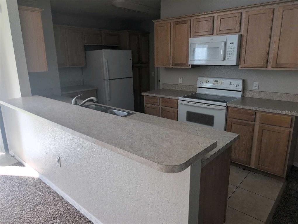 A kitchen features light wood cabinets, white appliances, and a laminate countertop breakfast bar — 2145 SANDY HOOK, LAKELAND, FL