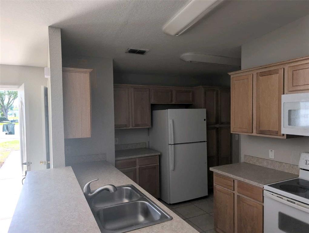 A kitchen features light wood cabinets, laminate countertops, a double sink, and white appliances — 2145 SANDY HOOK, LAKELAND, FL