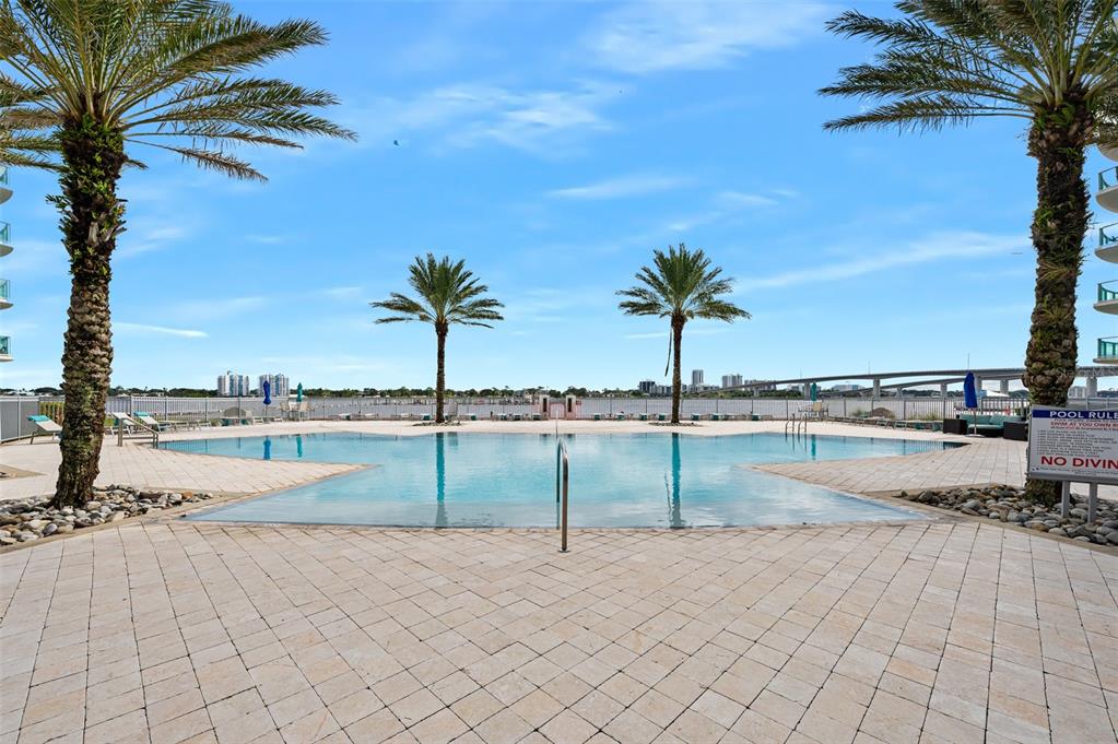 An outdoor swimming pool surrounded by palm trees and a paved deck overlooking a bridge — 231 RIVERSIDE DRIVE UNIT 1106-1, DAYTONA BEACH, FL