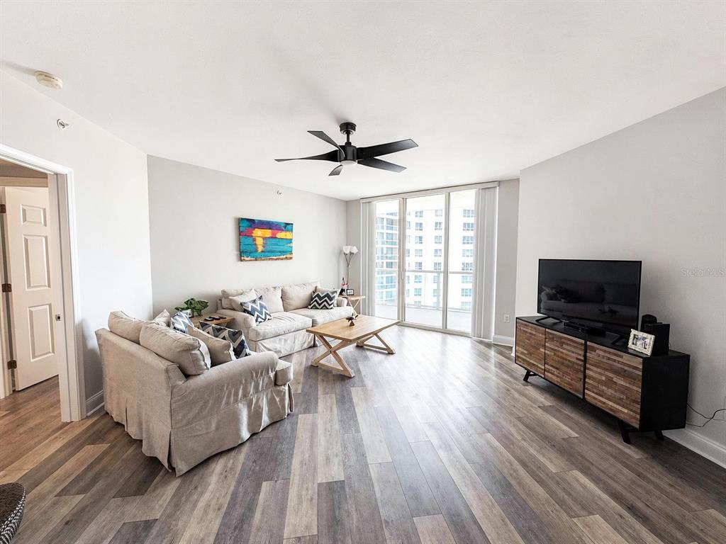 A living room features light gray walls, wood-look flooring, a ceiling fan, and floor-to-ceiling windows — 231 RIVERSIDE DRIVE UNIT 1106-1, DAYTONA BEACH, FL