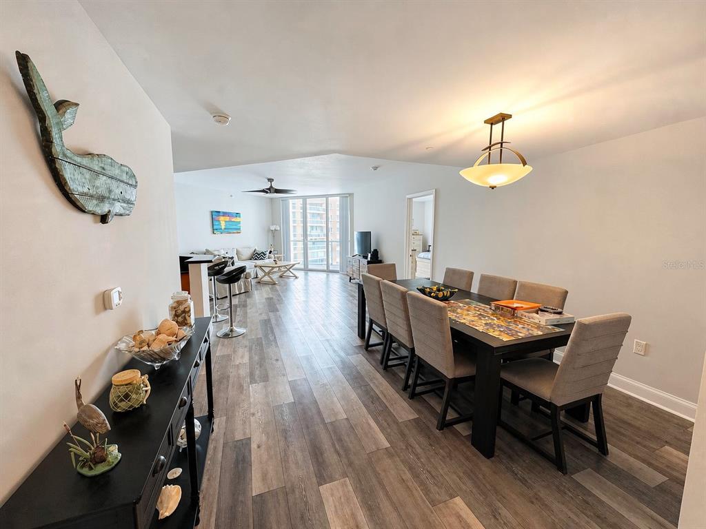 An open-concept dining and living area features wood-look flooring and a large wooden table — 231 RIVERSIDE DRIVE UNIT 1106-1, DAYTONA BEACH, FL