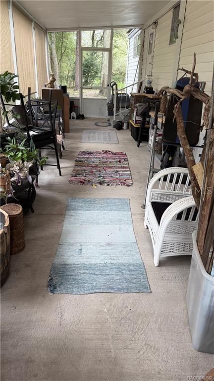 A screened-in porch features a concrete floor, multiple rugs, and a view of trees — 5282 W BLADE LANE, DUNNELLON, FL