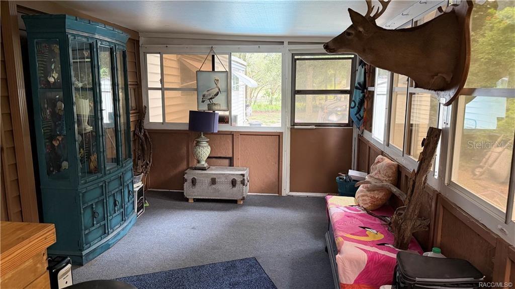 A screened-in porch features a blue cabinet, a deer mount, and a flamingo-patterned bench — 5282 W BLADE LANE, DUNNELLON, FL