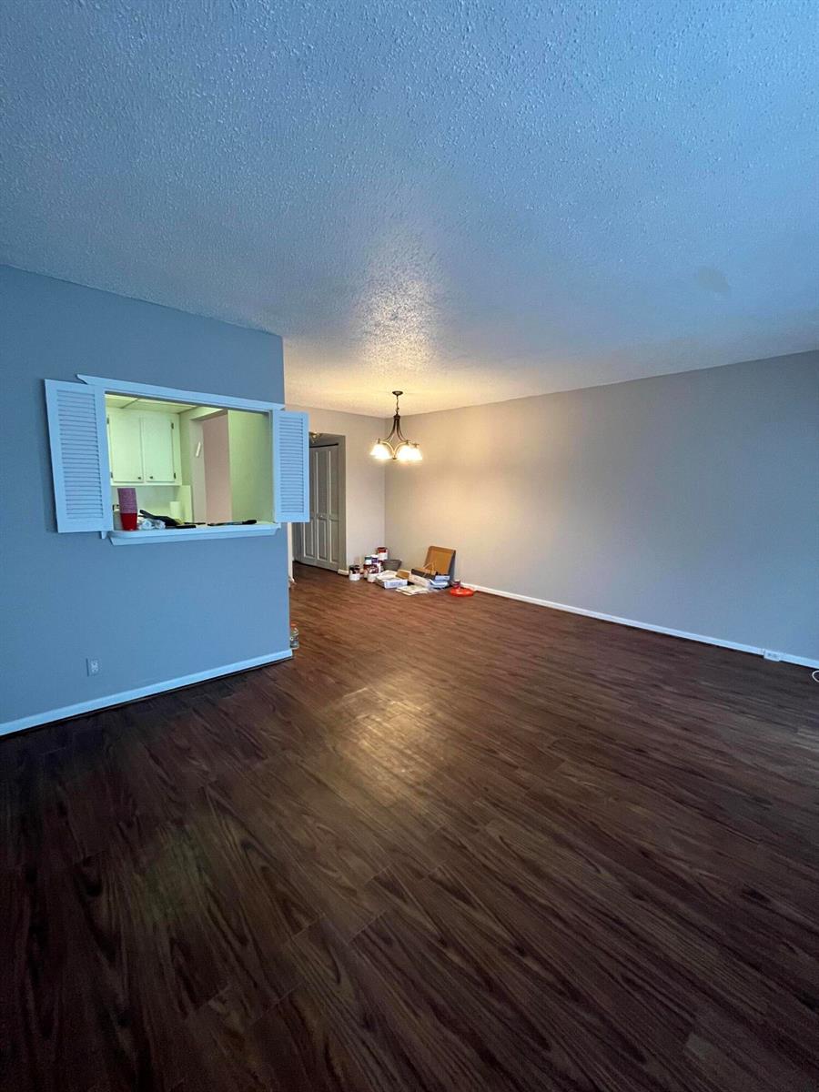 An empty room features dark wood-look flooring, gray walls, and a kitchen pass-through window — 119 E Westbury E # 119, Deerfield Beach FL 33442, DEERFIELD BEACH, FL