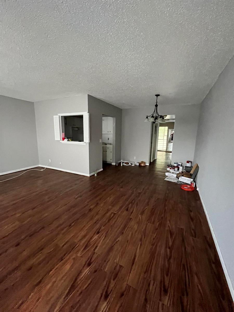 An empty living room features gray walls, dark wood-look flooring, and a pass-through window — 119 E Westbury E # 119, Deerfield Beach FL 33442, DEERFIELD BEACH, FL