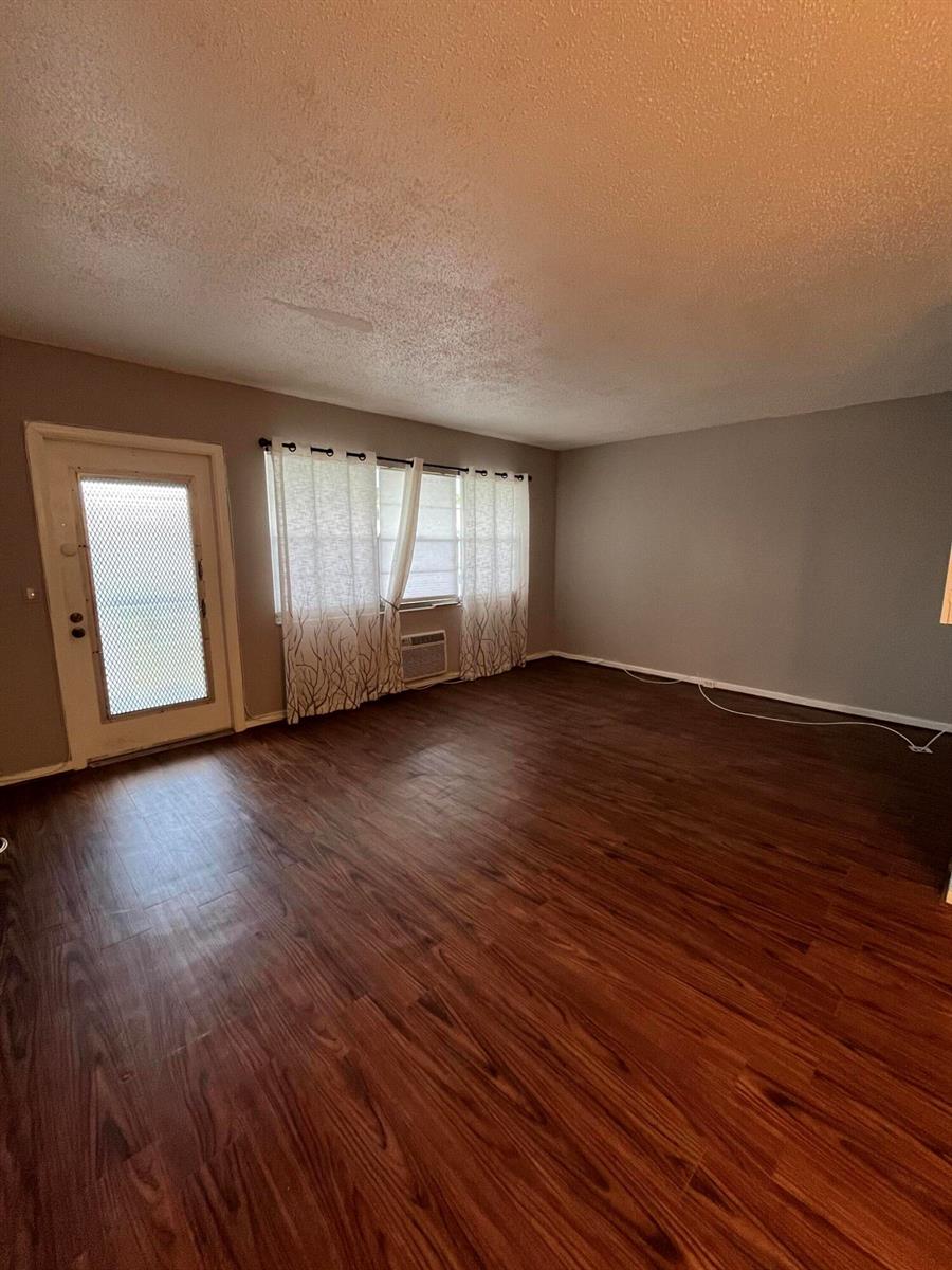An empty living room features dark wood-look flooring, gray walls, and a glass-paneled exterior door — 119 E Westbury E # 119, Deerfield Beach FL 33442, DEERFIELD BEACH, FL
