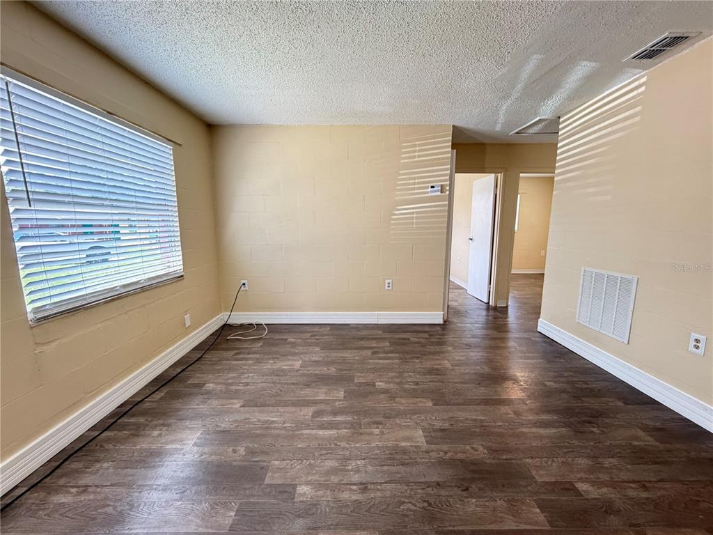 An empty room features tan block walls, dark wood-look flooring, and a window with blinds — 2988 STOWE PLACE, BARTOW, FL