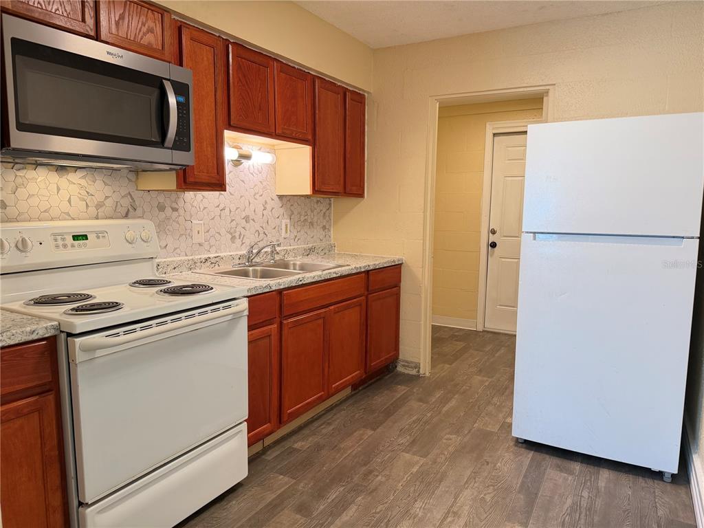 A kitchen features wood cabinets, white appliances, a patterned backsplash, and gray wood-look flooring — 2988 STOWE PLACE, BARTOW, FL