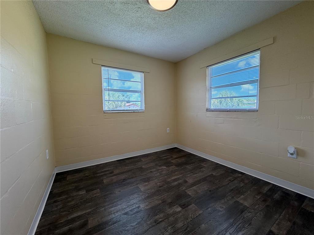 A bedroom with light yellow block walls, dark wood-look flooring, and two windows with blinds — 2988 STOWE PLACE, BARTOW, FL