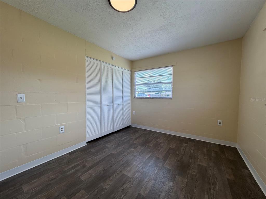 A bedroom with light-colored block walls, dark wood-look flooring, and white louvered closet doors — 2988 STOWE PLACE, BARTOW, FL