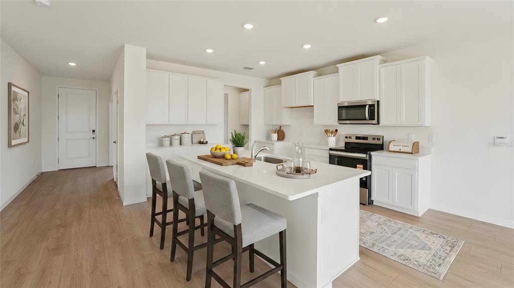 A modern kitchen features white cabinets, a central island with bar seating, and light flooring — 17979 NW 172ND AVENUE, ALACHUA, FL