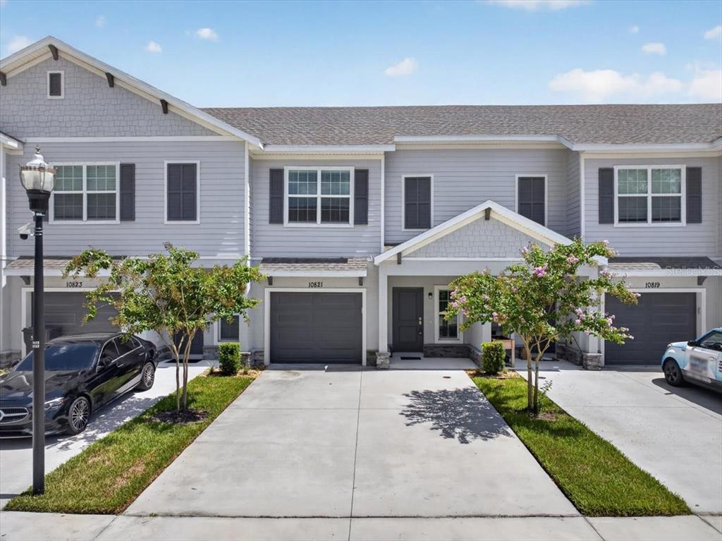 A row of three attached townhouses with gray siding, concrete driveways, and small front trees — 10821 QUICKWATER COURT, RIVERVIEW, FL