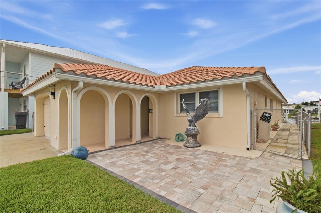 A beige house with a tiled roof, arched entryway, and a paved patio area — 4549 TOPSAIL TRAIL, NEW PORT RICHEY, FL