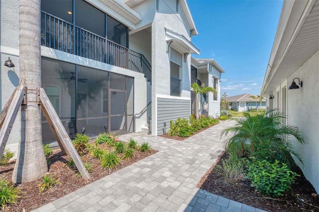 A paved walkway leads between a two-story building with screened balconies and a neighboring structure — 12470 WELLEN GOLF STREET UNIT 207, VENICE, FL