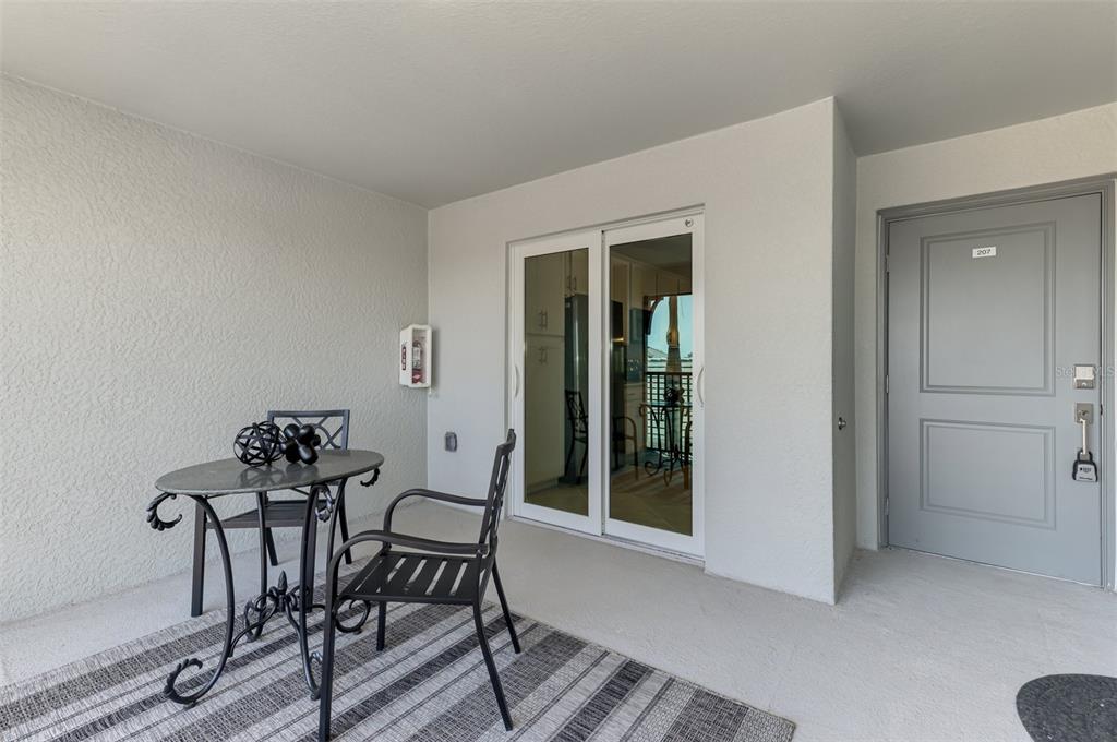 A covered balcony features a small metal bistro set, a sliding glass door, and a door — 12470 WELLEN GOLF STREET UNIT 207, VENICE, FL