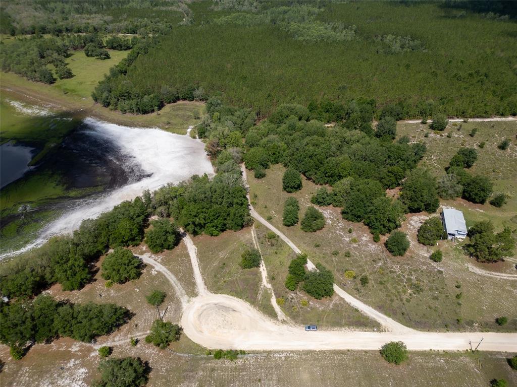 An aerial view shows a dirt cul-de-sac, a small house, trees, and a large pond — SE 53 COURT, TRENTON, FL