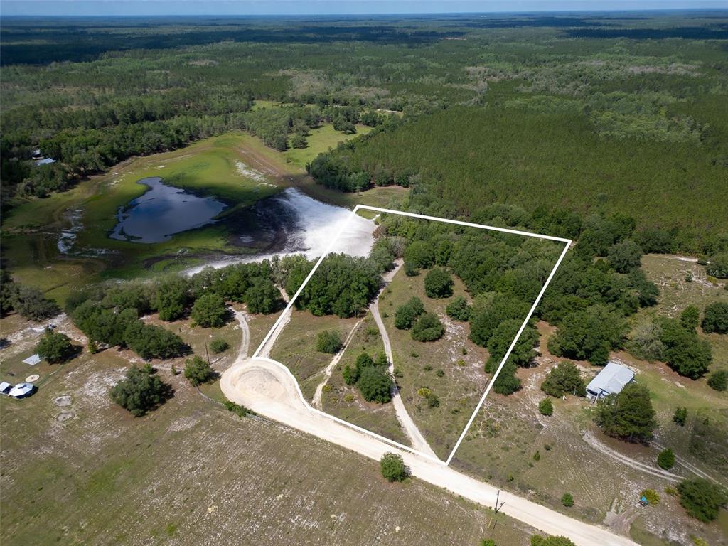 An aerial view shows a vacant, partially wooded lot outlined in white near a pond — SE 53 COURT, TRENTON, FL