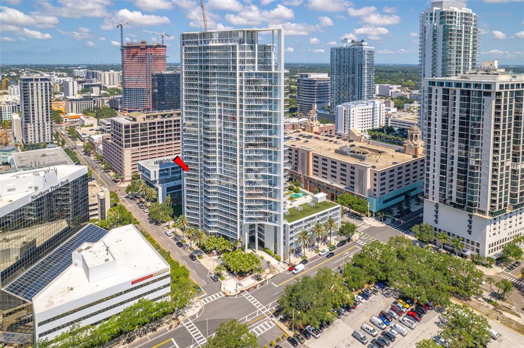 An aerial view of a tall residential skyscraper surrounded by city buildings and parking lots — 175 1ST STREET S UNIT 1204, ST PETERSBURG, FL