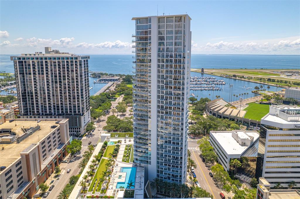 An aerial view shows a tall residential skyscraper next to a marina and airport runway — 175 1ST STREET S UNIT 1204, ST PETERSBURG, FL