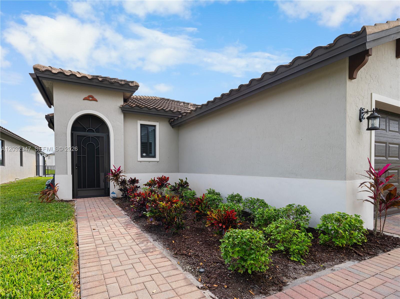 The exterior of a house features a brick walkway, a front door, and landscaped garden beds — 5028 Arancia Lane, Ave Maria FL 34142, AVE MARIA, FL