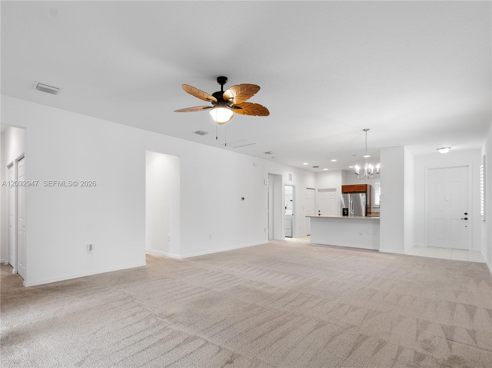 A spacious living room features beige carpeting, a ceiling fan, and an open kitchen area — 5028 Arancia Lane, Ave Maria FL 34142, AVE MARIA, FL