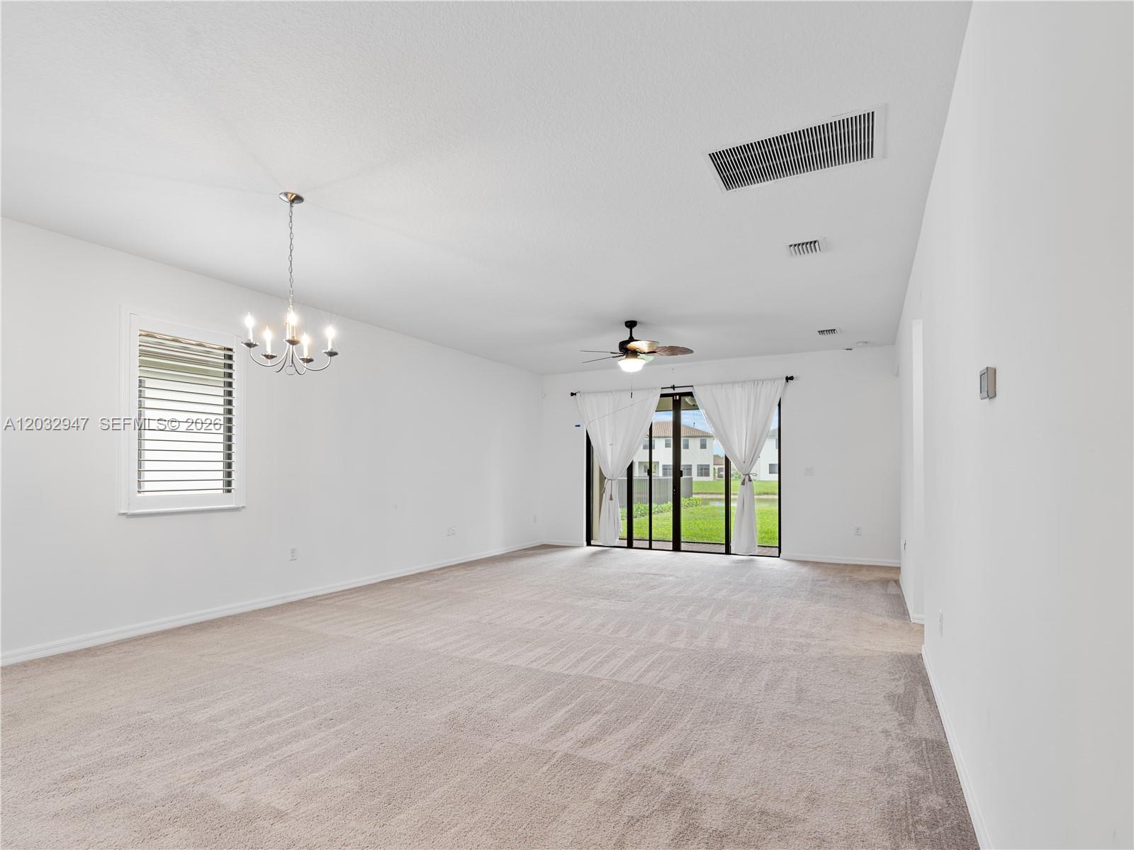 A spacious, carpeted living room features white walls, a ceiling fan, and sliding glass doors — 5028 Arancia Lane, Ave Maria FL 34142, AVE MARIA, FL