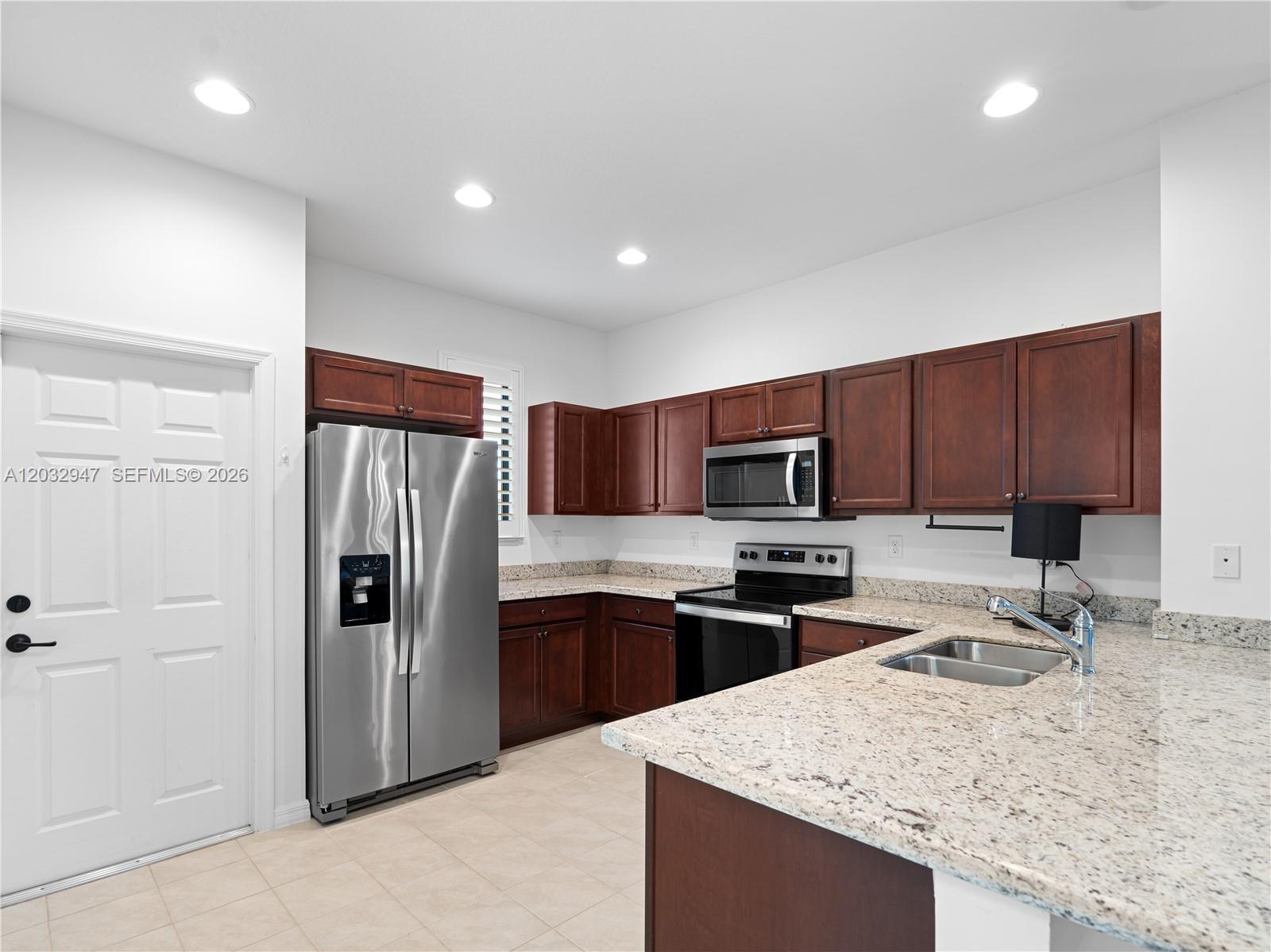 A kitchen features dark wood cabinets, granite countertops, and stainless steel appliances — 5028 Arancia Lane, Ave Maria FL 34142, AVE MARIA, FL