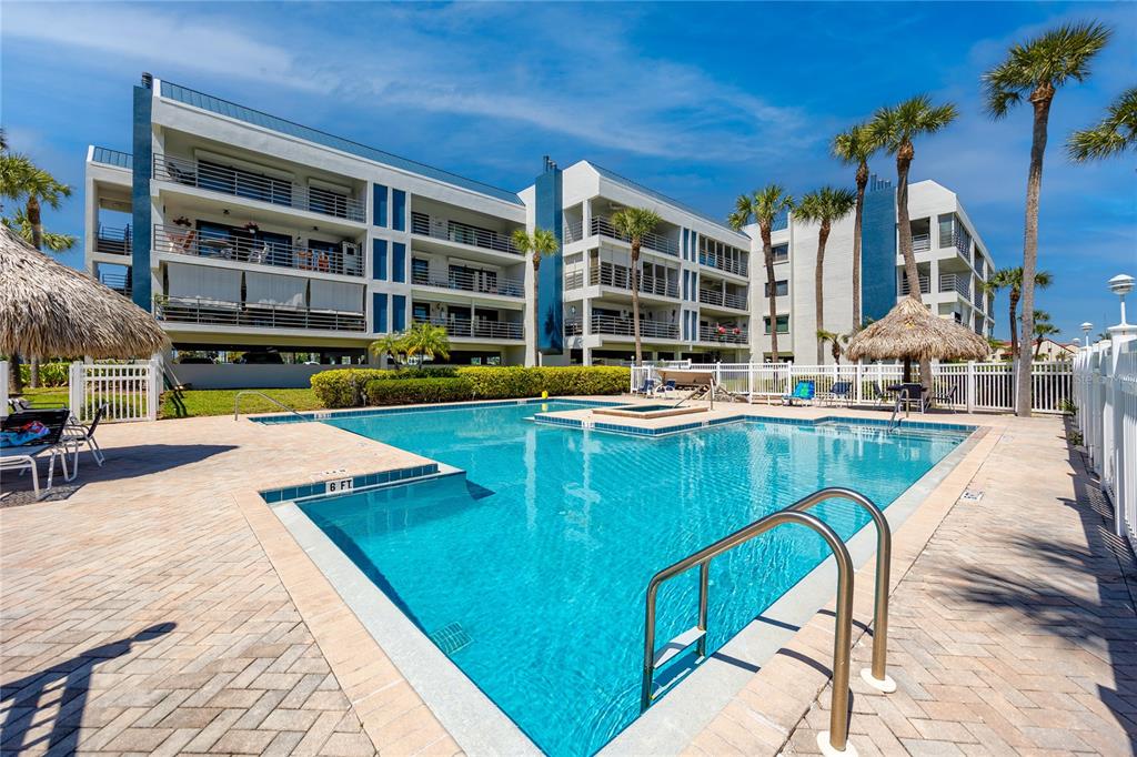 A multi-story apartment building overlooks a swimming pool with a surrounding patio and palm trees — 363 PINELLAS BAYWAY S UNIT 48, TIERRA VERDE, FL