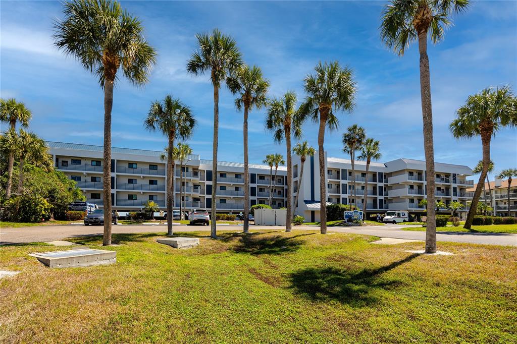 A multi-story apartment building stands behind a grassy lawn with several tall palm trees — 363 PINELLAS BAYWAY S UNIT 48, TIERRA VERDE, FL