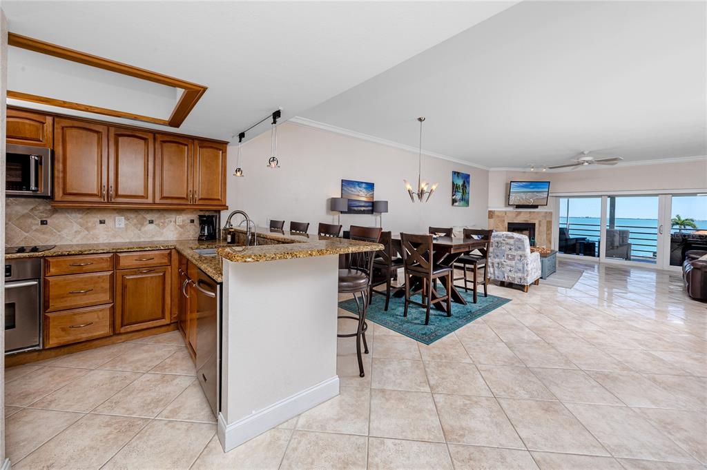 A kitchen with wood cabinets and granite countertops opens to a dining area and living room — 363 PINELLAS BAYWAY S UNIT 48, TIERRA VERDE, FL