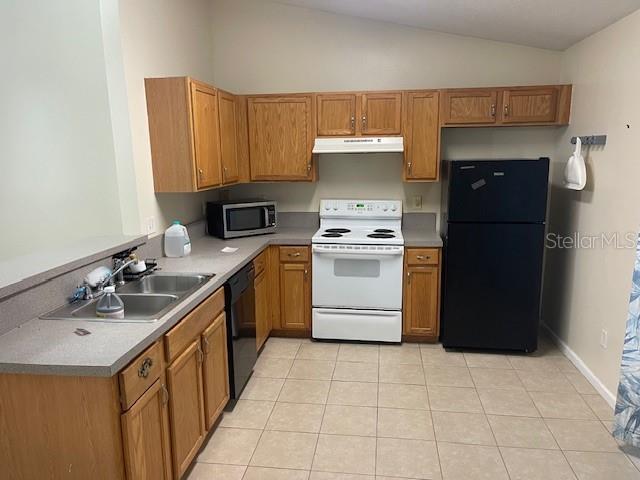 A kitchen features oak cabinets, a white stove, a black refrigerator, and tile flooring — 38 PINE HURST LANE UNIT B, PALM COAST, FL