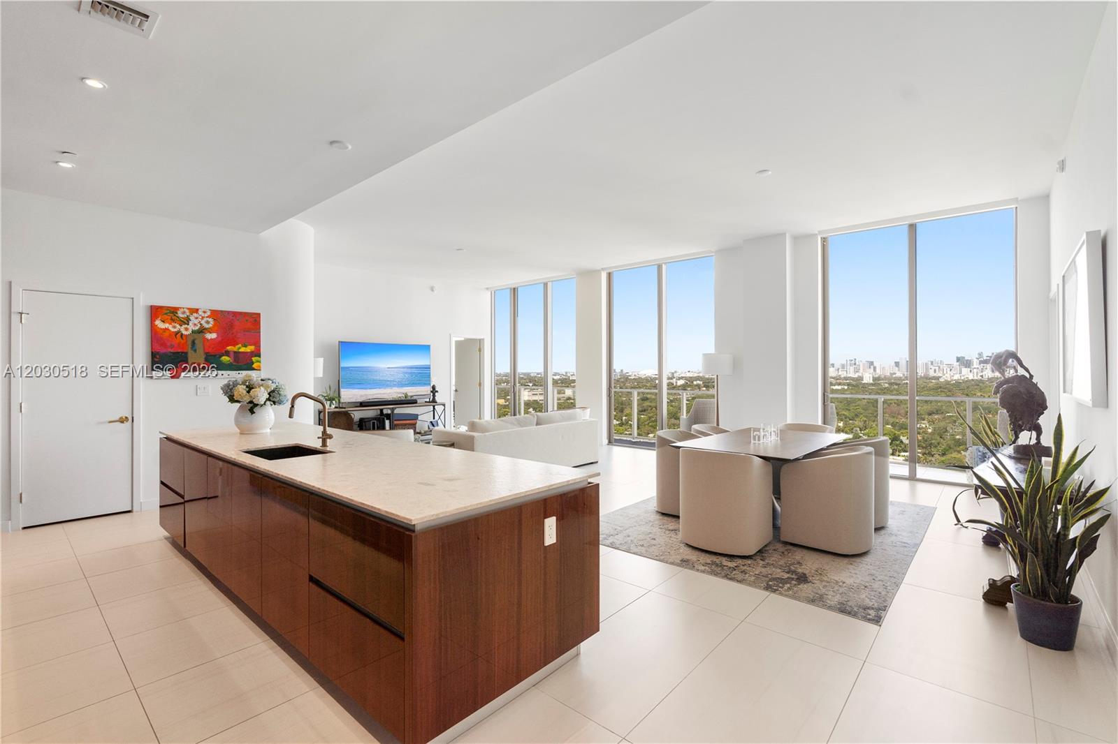 A modern open-concept kitchen and dining area features wood cabinetry, stone countertops, and floor-to-ceiling windows — 2678 Tigertail Ave, Miami FL 33133, MIAMI, FL