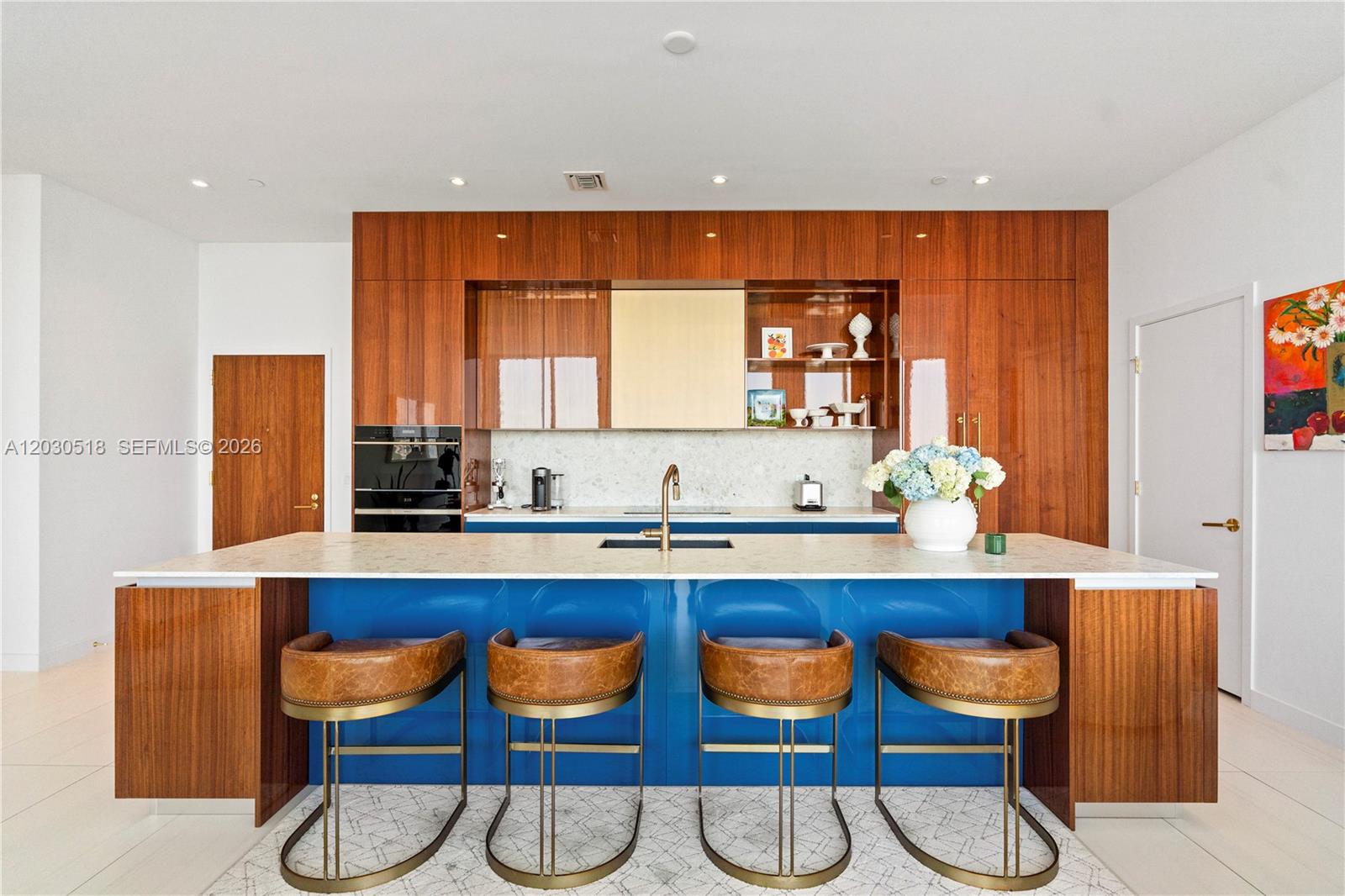 A modern kitchen features a blue island with leather stools against wood-paneled cabinetry — 2678 Tigertail Ave, Miami FL 33133, MIAMI, FL