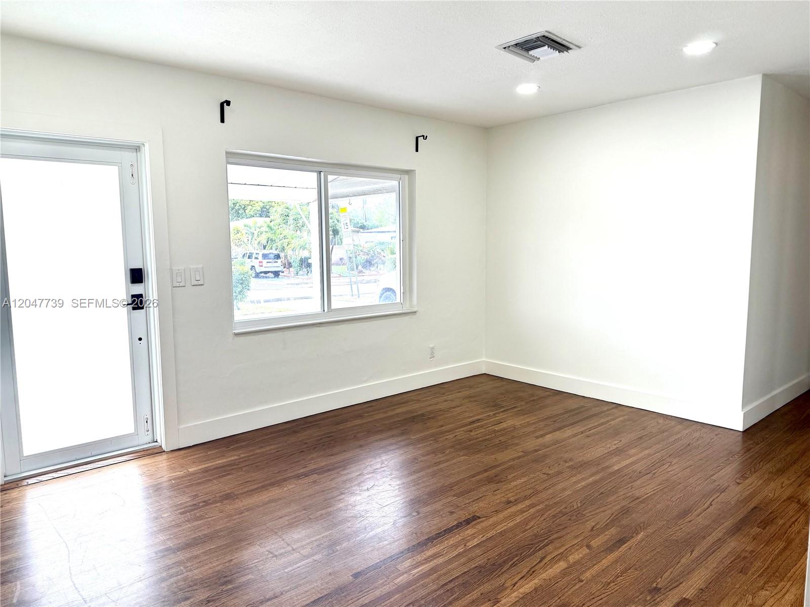 An empty room features white walls, dark wood flooring, a window, and a glass door — 670 E 58th St, Hialeah FL 33013, HIALEAH, FL