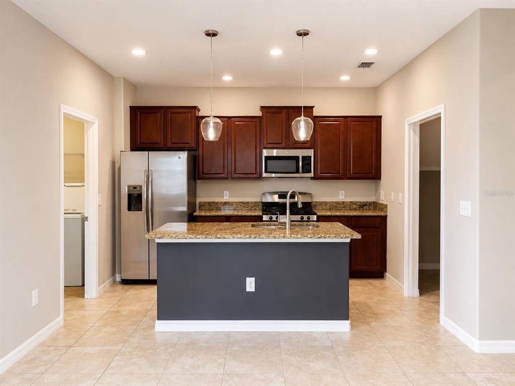 A kitchen features dark wood cabinets, granite countertops, a central island, and stainless steel appliances — 17575 BRIGHTON LAKE ROAD, LAND O LAKES, FL