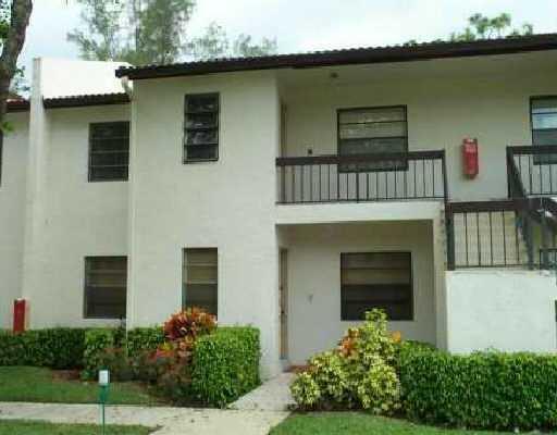 A two-story apartment building with a balcony, dark railings, and manicured hedges in front — 21614 Juego Circle # 25h, Boca Raton FL 33433, BOCA RATON, FL