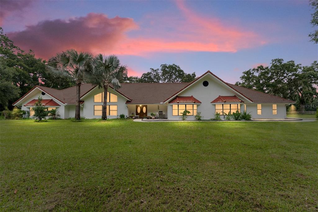 A single-story house with a tiled roof and large windows sits on a grassy lawn — 553 NE 205TH AVENUE, WILLISTON, FL