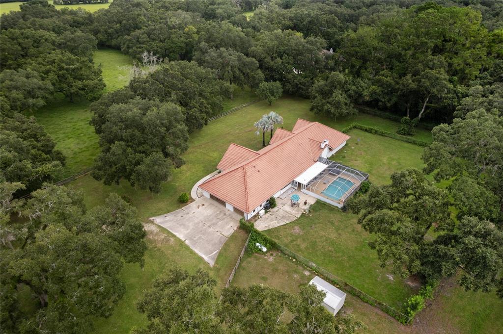 An aerial view shows a house with a tiled roof, pool, and surrounding wooded property — 553 NE 205TH AVENUE, WILLISTON, FL