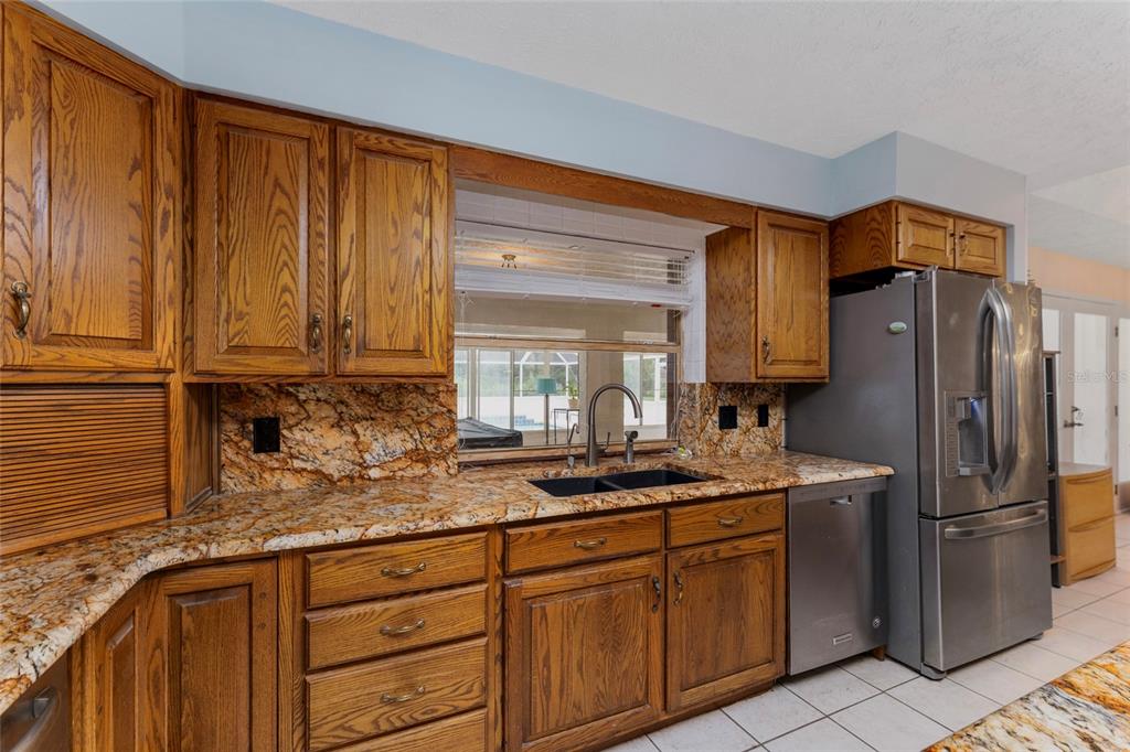 A kitchen features oak cabinets, granite countertops, a stainless steel refrigerator, and a sink window — 553 NE 205TH AVENUE, WILLISTON, FL