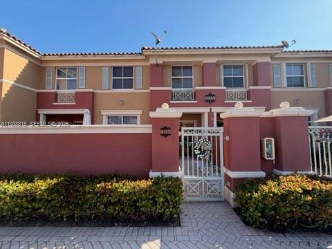 A two-story townhouse exterior features a gated courtyard, reddish-brown stucco walls, and white trim — 6015 NW 116th Pl # 465, Doral FL 33178, DORAL, FL