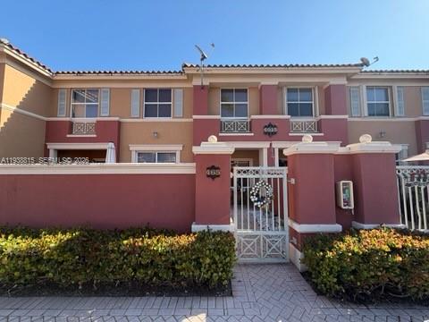 A two-story townhouse exterior features a gated courtyard, reddish-brown walls, and a paved walkway — 6015 NW 116th Pl # 465, Doral FL 33178, DORAL, FL