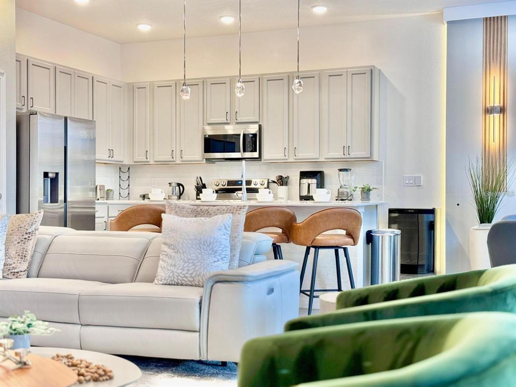A modern kitchen with light gray cabinets and a breakfast bar overlooks a living area — 10012 VOYAGER WAY, ORLANDO, FL